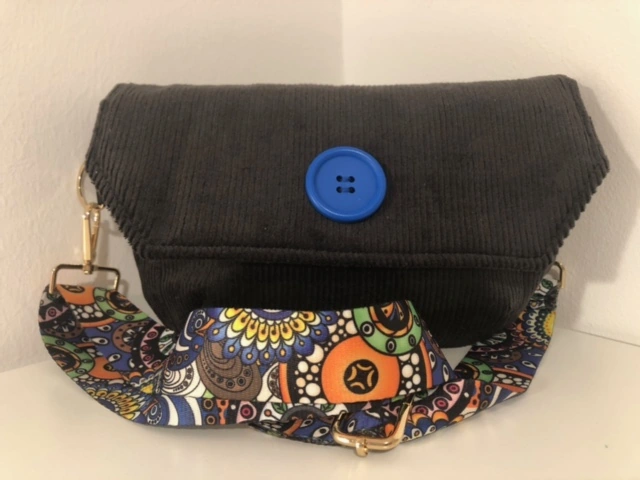 Schwarze Nachtschwärmerin aus Cord mit blauem Knopf und bunt gemustertem Schultergurt